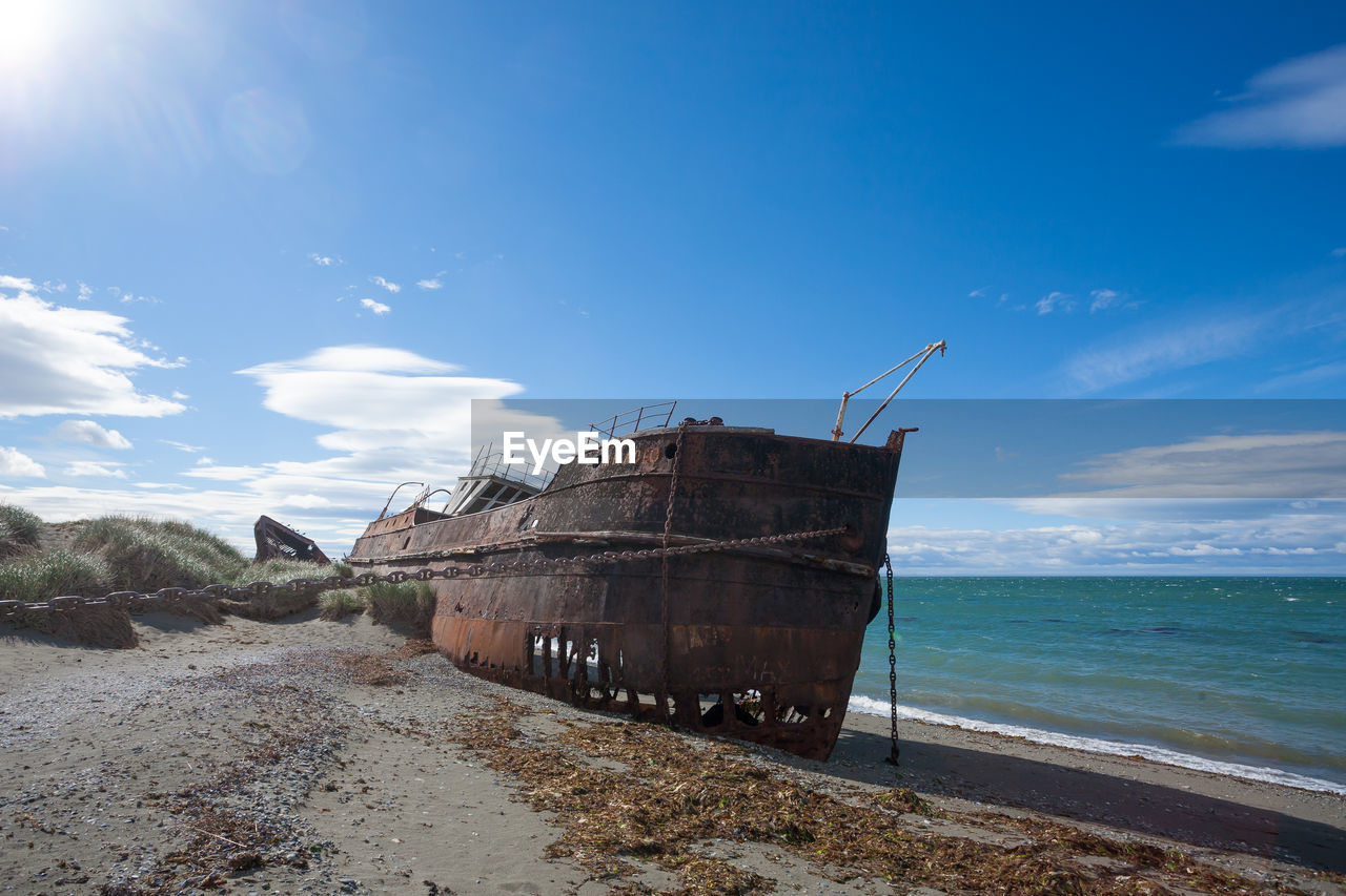 ABANDONED BOAT ON BEACH AGAINST BLUE SKY