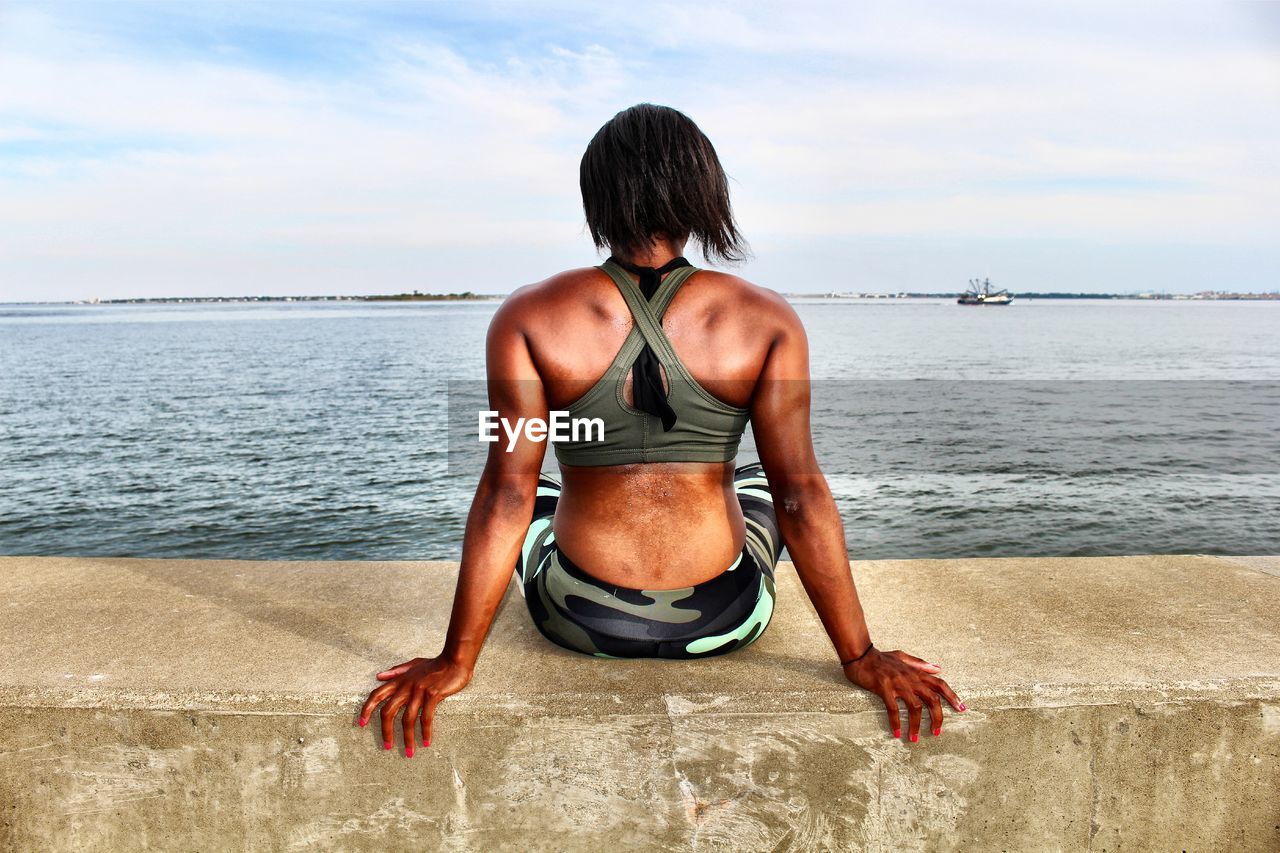 REAR VIEW OF SHIRTLESS MAN ON SEA SHORE