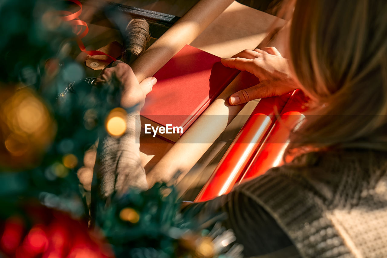 Blond woman wrapping presents in recycled card and decorated it with dried oranges and fir branches.