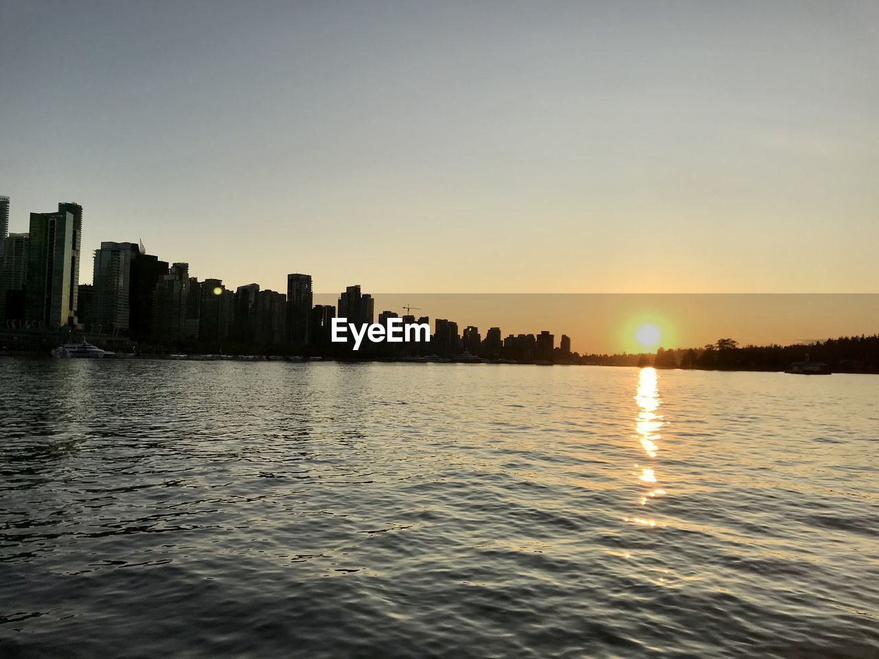 SEA BY BUILDINGS AGAINST CLEAR SKY DURING SUNSET