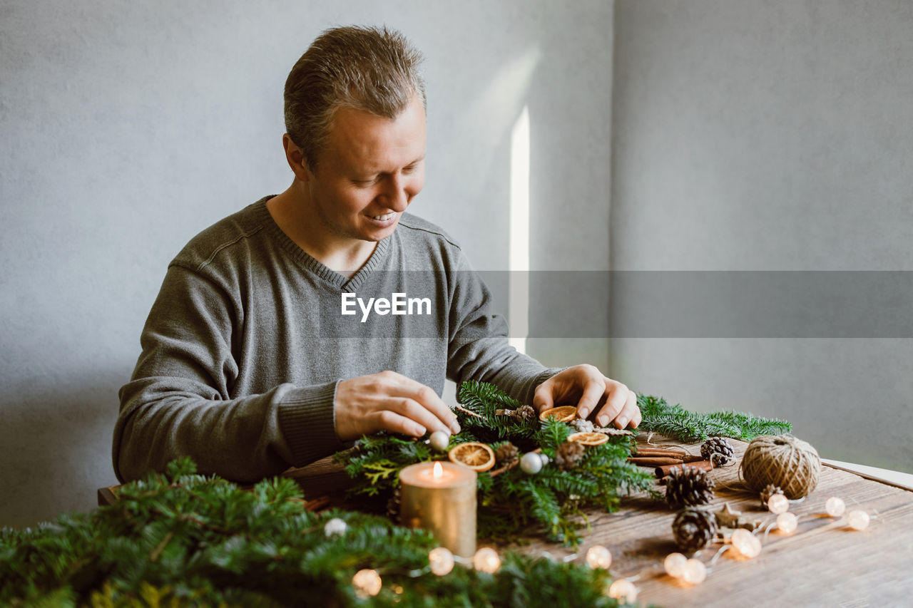 A male florist makes a new year's wreath with fresh fir branches, pine cones and dried fruits. 