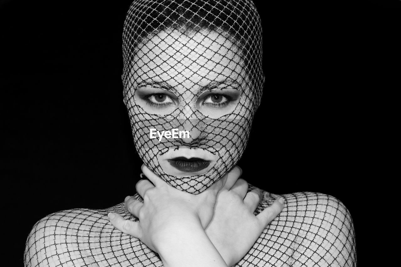 Portrait of young woman covered with net against black background