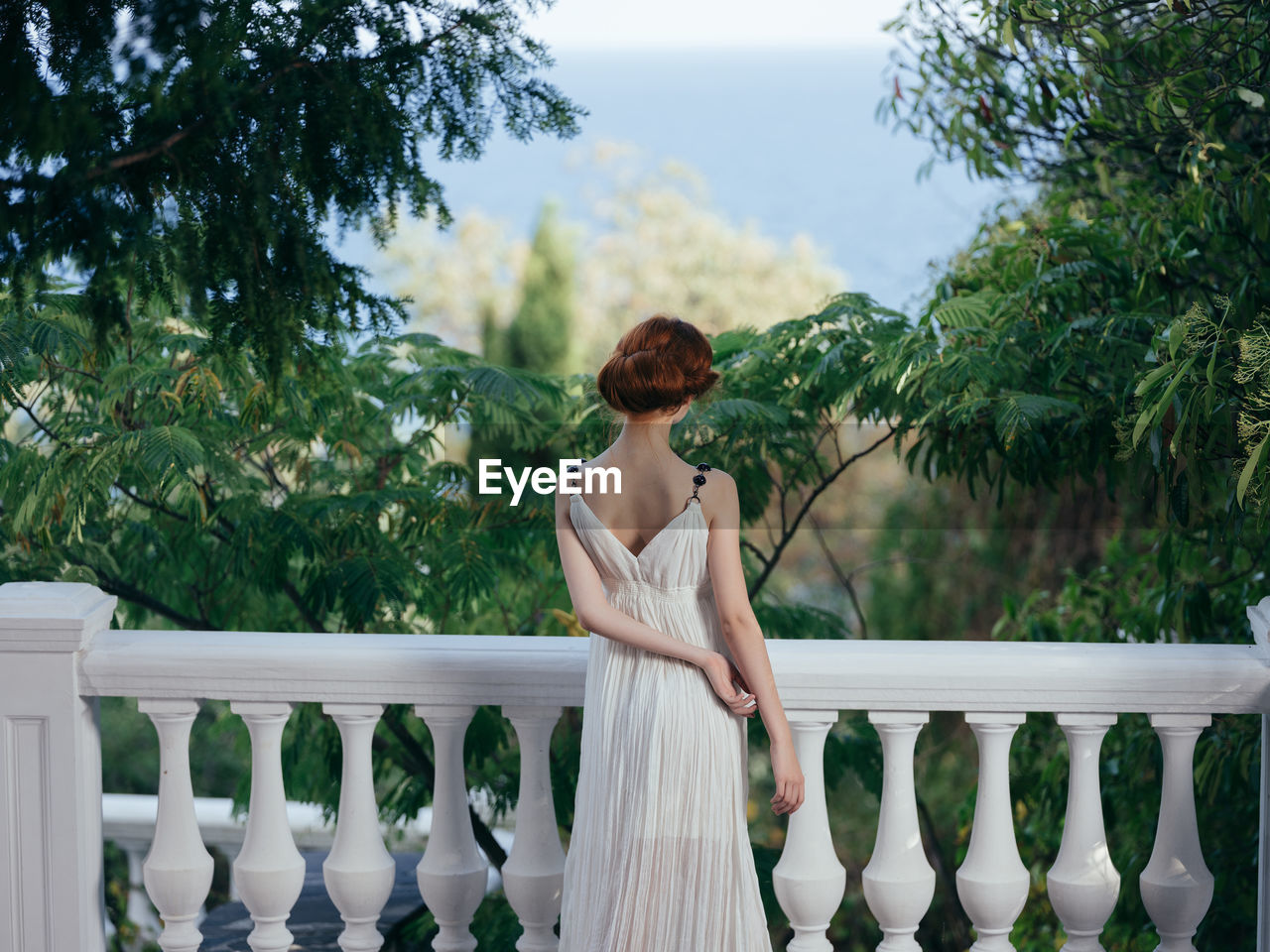 WOMAN STANDING ON RAILING AGAINST TREES