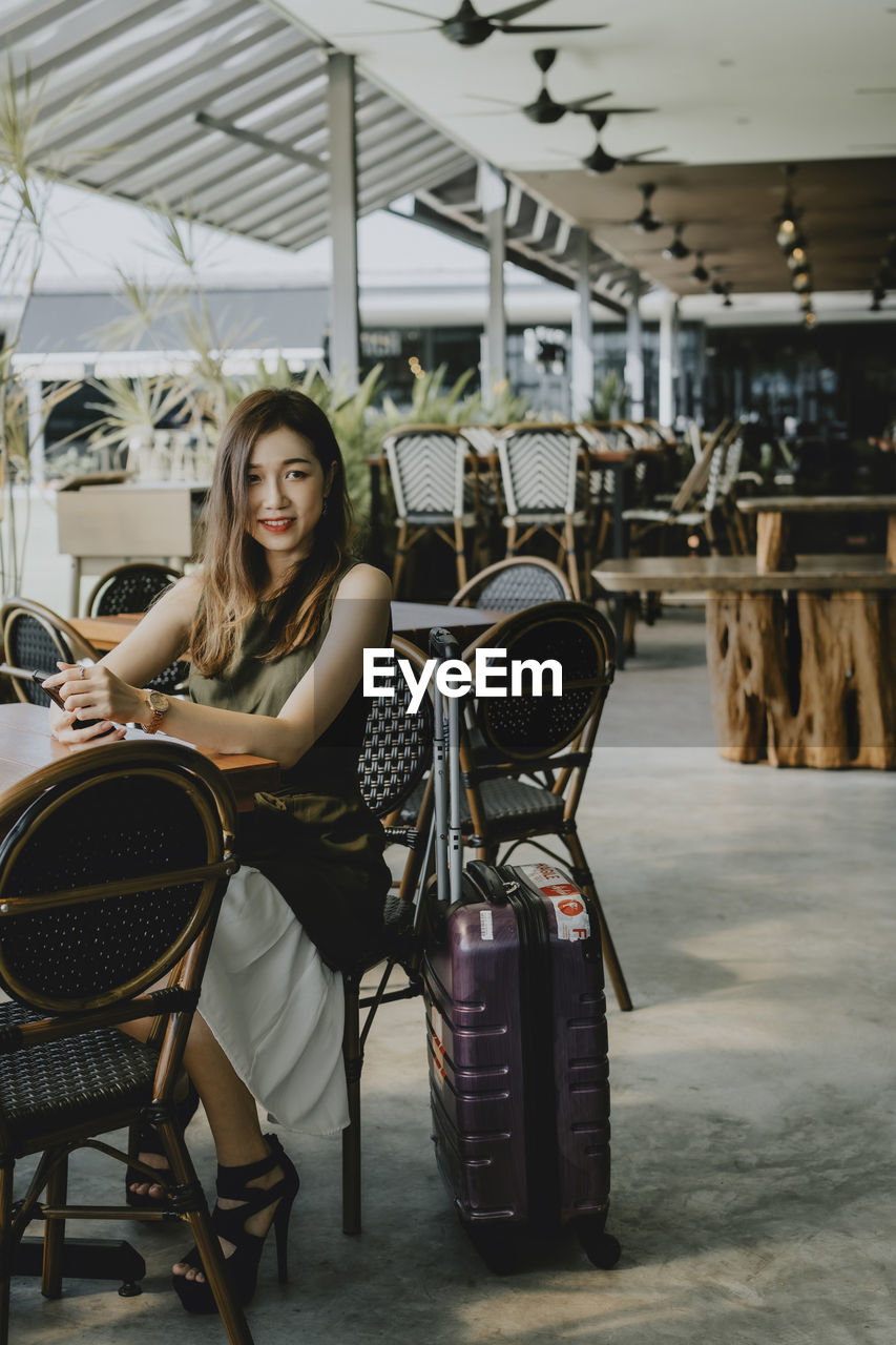 Portrait of young woman sitting on chair at outdoor cafe