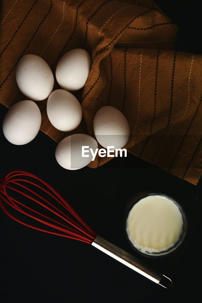 Directly above shot of eggs and milk with whisk against black background