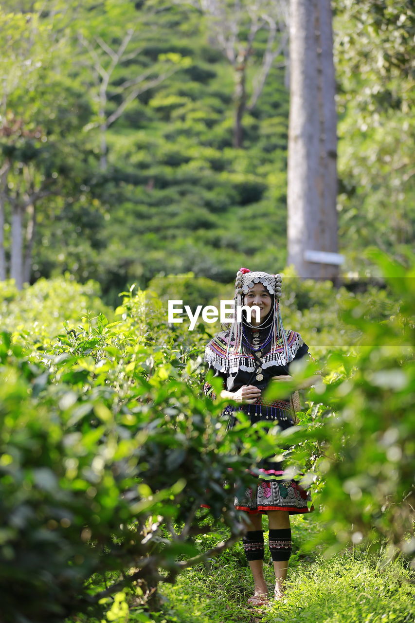 YOUNG WOMAN STANDING BY TREE