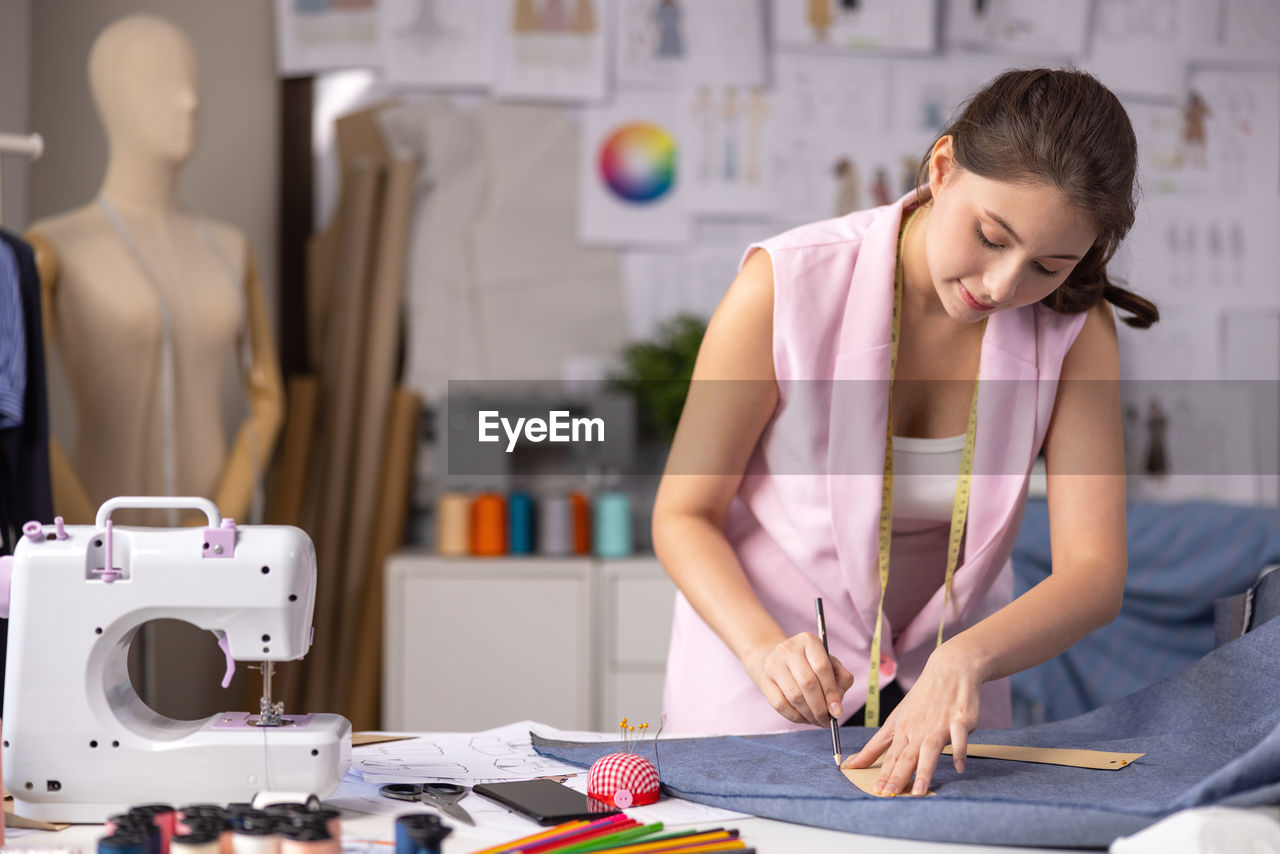 In her workplace, an asian tailor modifies the design of a garment on a mannequin.