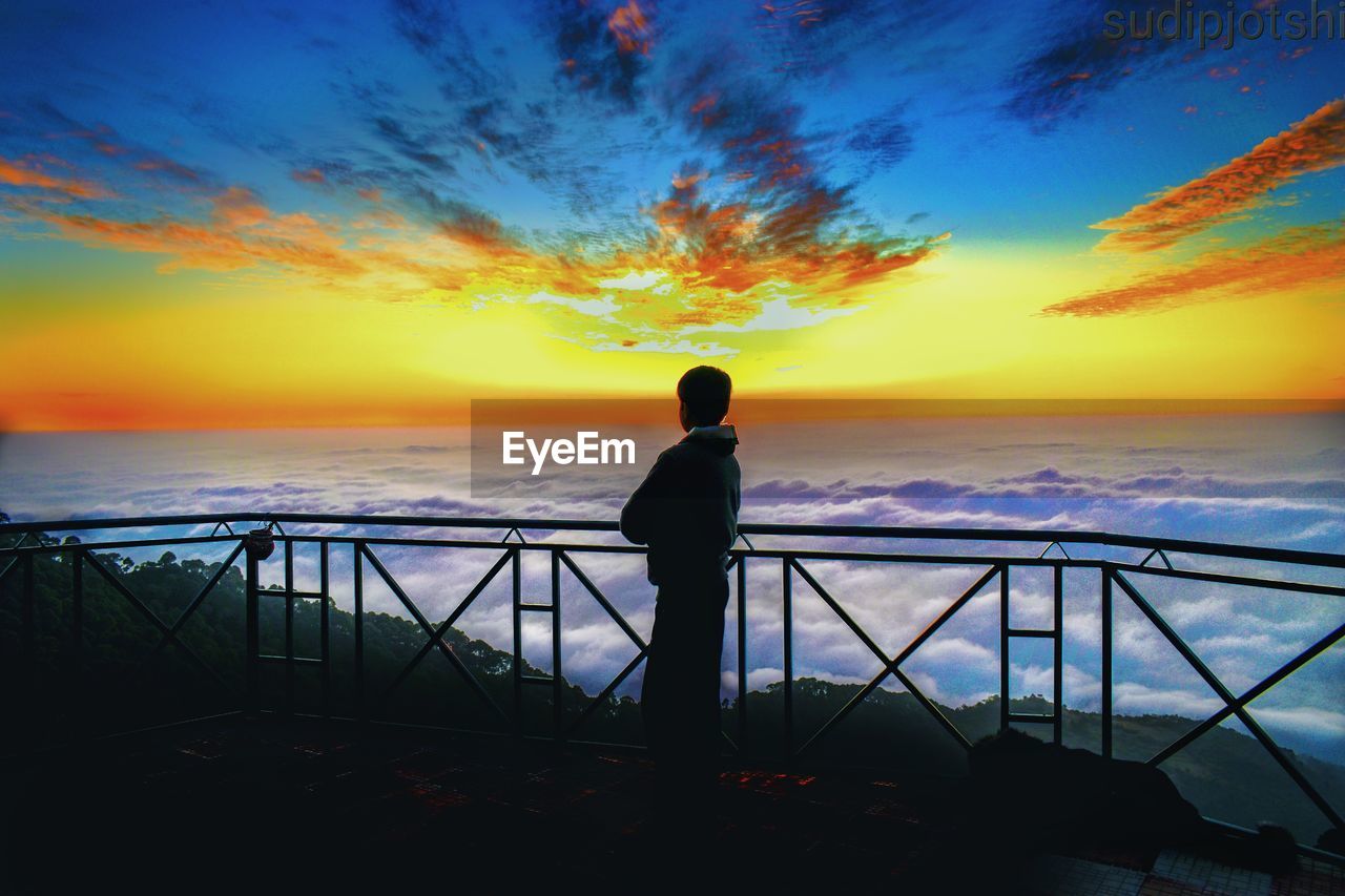 sky, sunset, sea, horizon, water, ocean, evening, one person, silhouette, beauty in nature, sunlight, cloud, nature, dusk, scenics - nature, beach, railing, horizon over water, standing, reflection, land, men, tranquility, adult, rear view, orange color, full length, tranquil scene, vacation, afterglow, trip, coast, idyllic, leisure activity, looking at view, architecture, outdoors, holiday, shore, travel, lifestyles, travel destinations, urban skyline, wave, relaxation, dramatic sky, sun