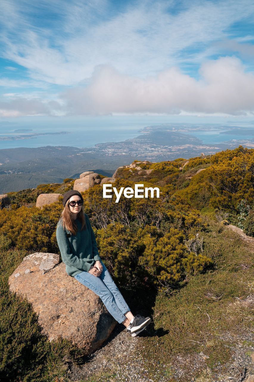 Portrait of smiling woman sitting on mountain against sky