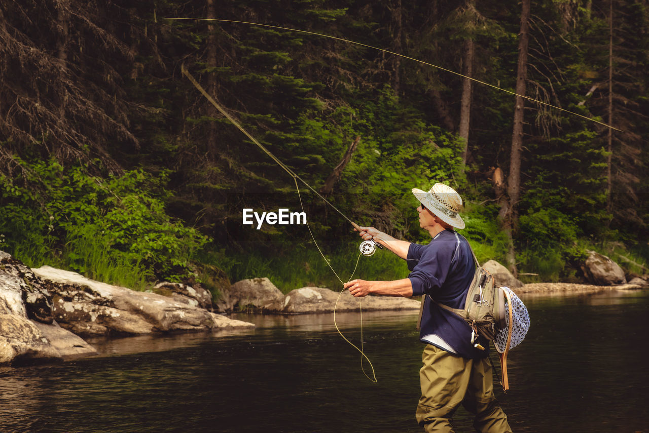 Rear view of man wearing hat fishing in river