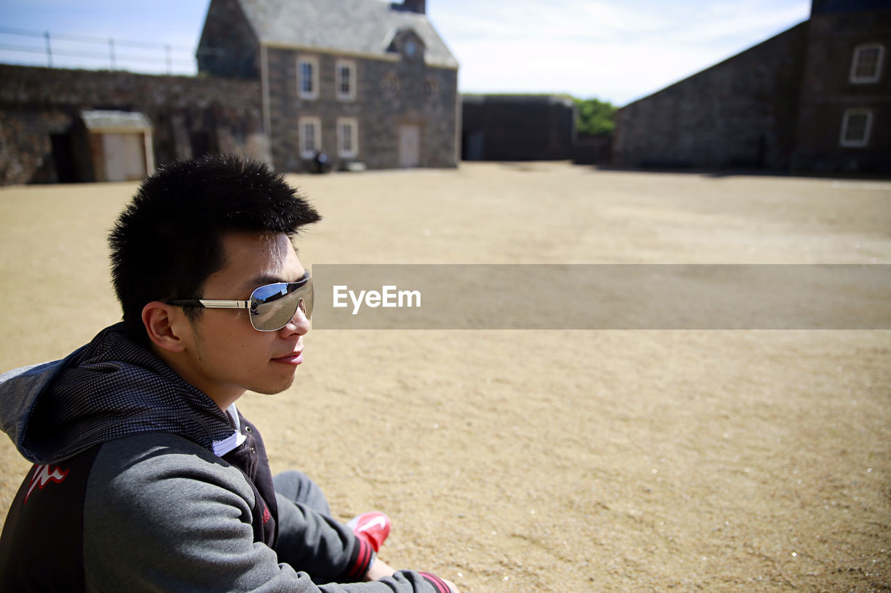 Young man sitting on sand outside historic castle