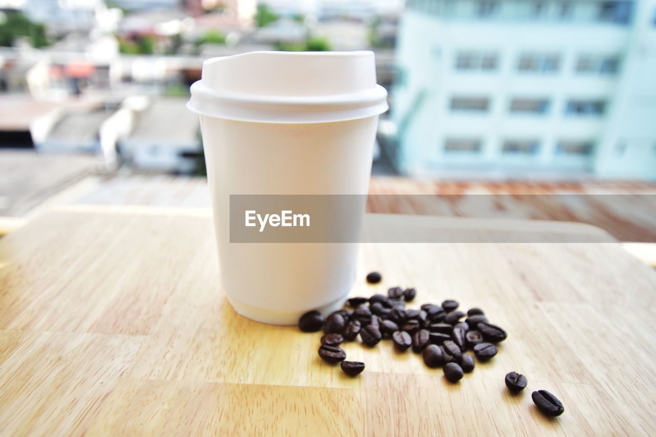 Close-up of disposable cup and coffee beans on table