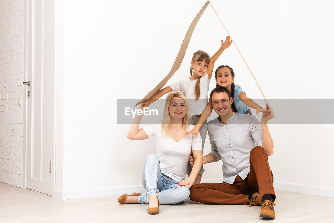 PORTRAIT OF SMILING YOUNG COUPLE SITTING ON WOODEN FLOOR