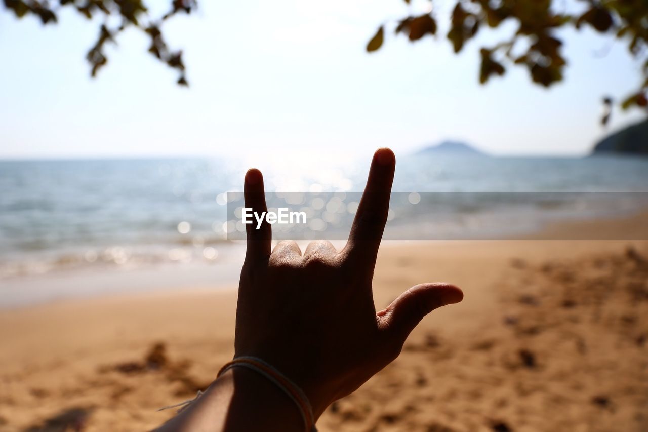 Cropped hand showing rock sign at beach