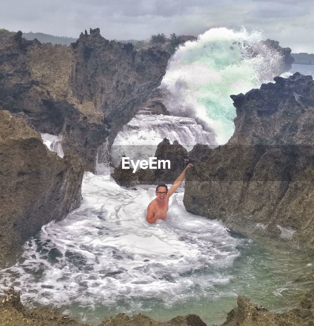 Shirtless man swimming in sea by rock formation