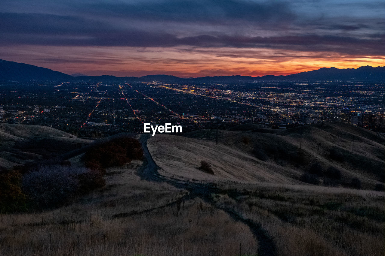 HIGH ANGLE VIEW OF ILLUMINATED CITYSCAPE AGAINST SKY DURING SUNSET