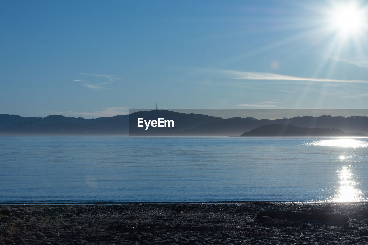 SCENIC VIEW OF SEA AND MOUNTAINS AGAINST BRIGHT SUN