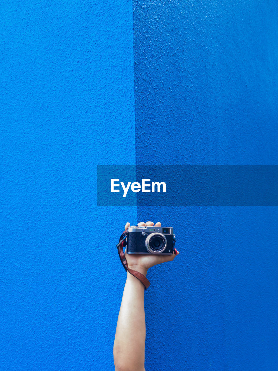 Cropped image of person holding vintage camera against blue wall