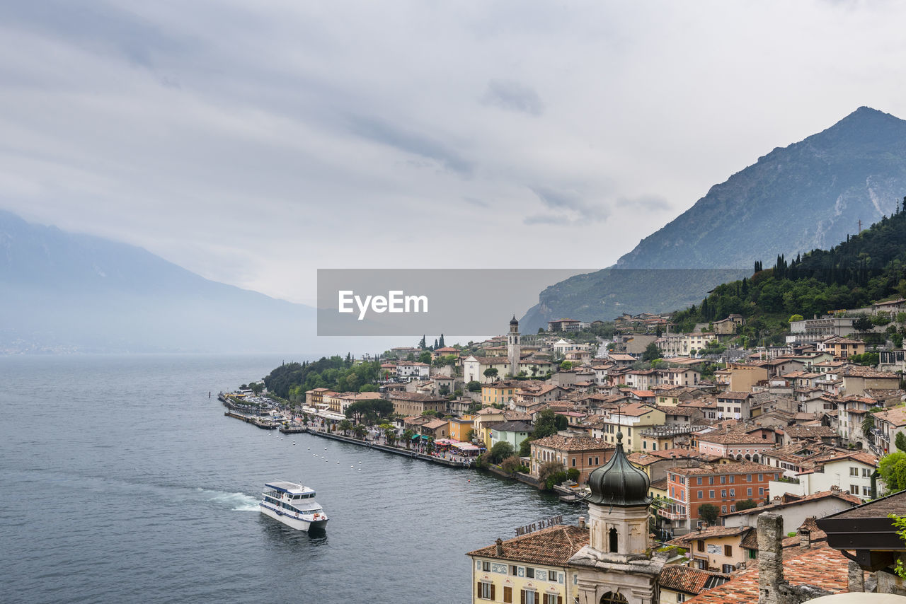 Residential district by lake and mountains against cloudy sky