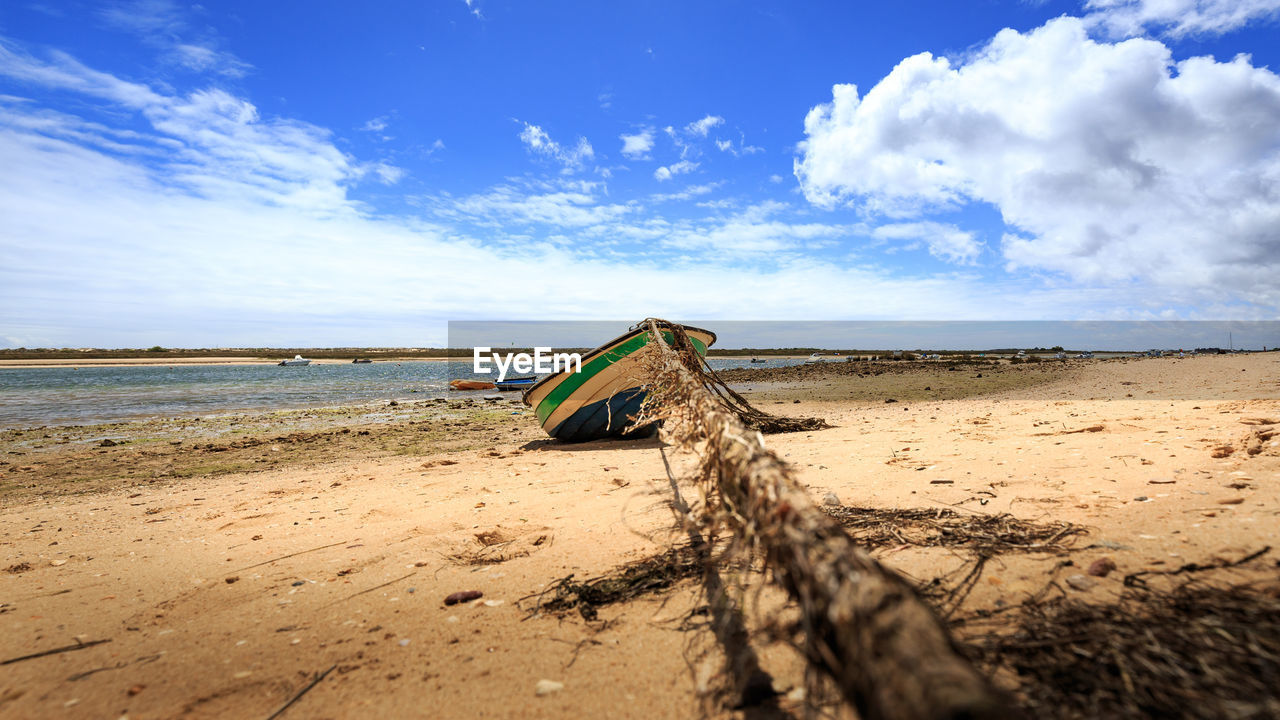 Fishing boat moored at beach against cloudy sky