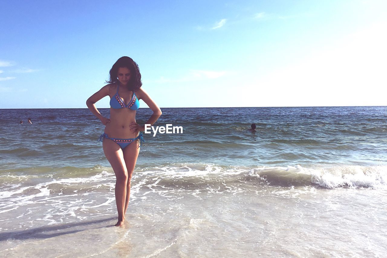 Full length of woman in bikini walking on shore against sky