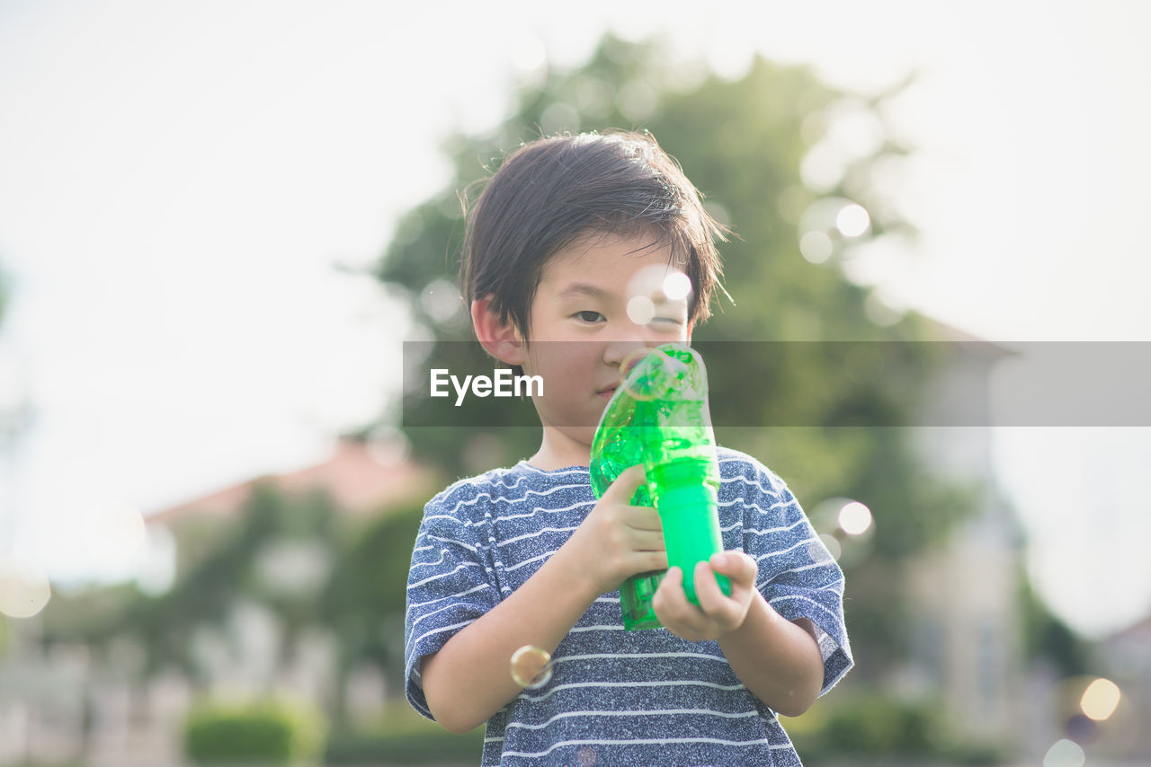 Cute boy blowing bubbles with gun against tree