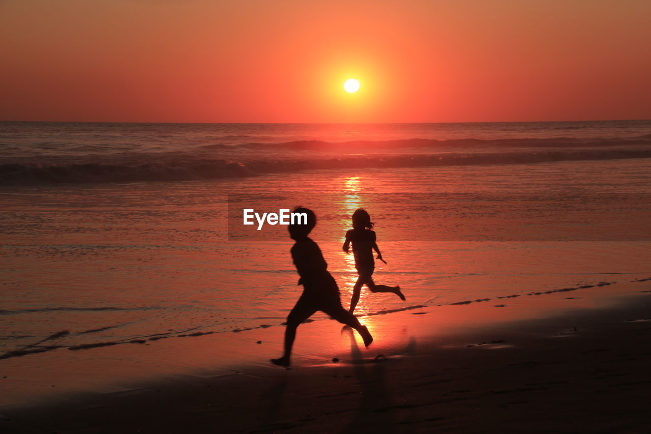 SILHOUETTE MEN ON BEACH AGAINST ORANGE SKY