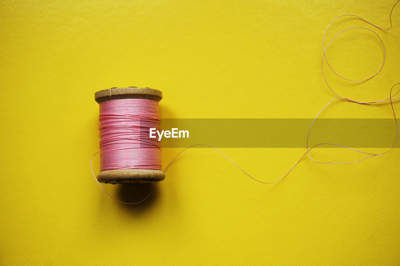 High angle view of thread spool over yellow background