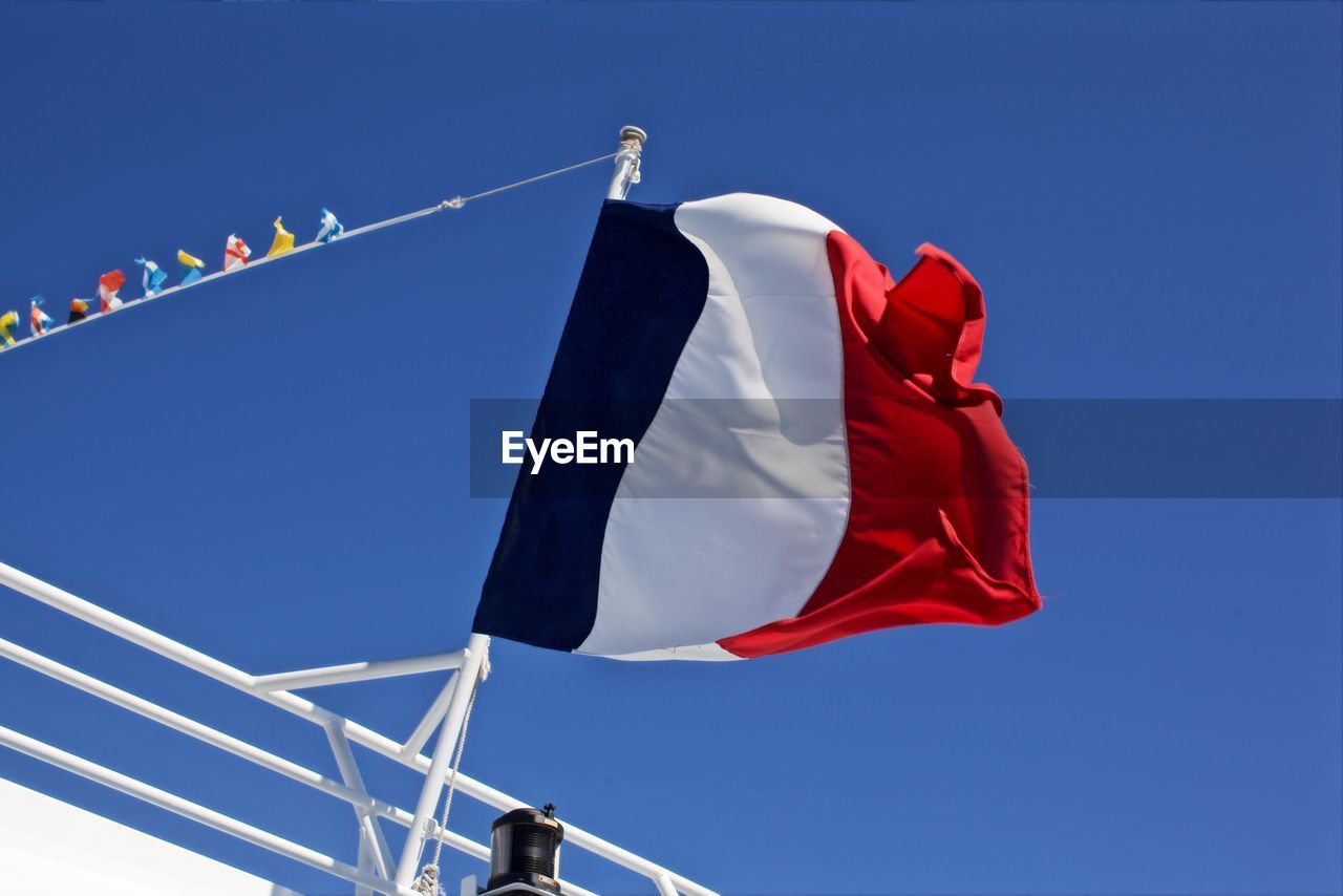 Low angle view of french flag on railing against clear blue sky