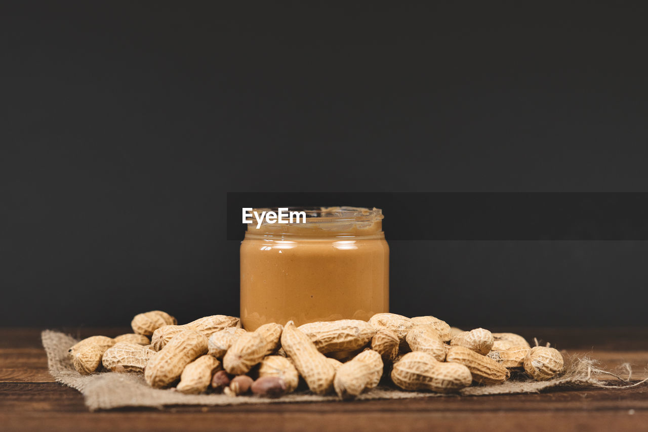 Close-up of peanut butter in jar with peanut butter on table against black background 