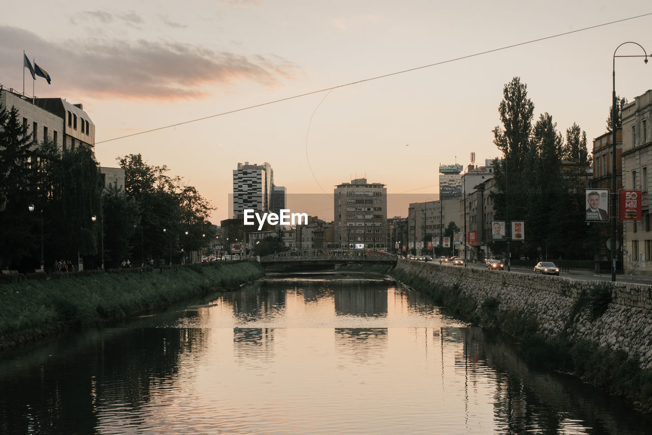 REFLECTION OF BUILDINGS IN CITY ON RIVER DURING SUNSET