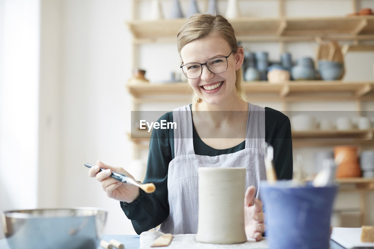 Portrait of smiling young woman learning pottery in art studio