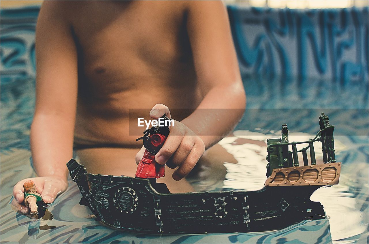 Midsection of shirtless boy playing with toy while sitting in swimming pool