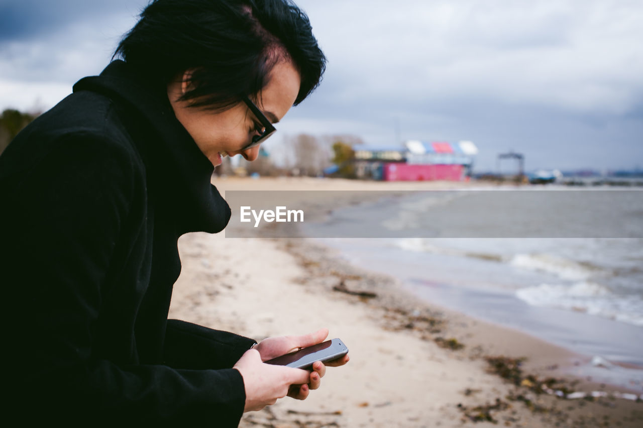 Woman using mobile phone at beach against sky