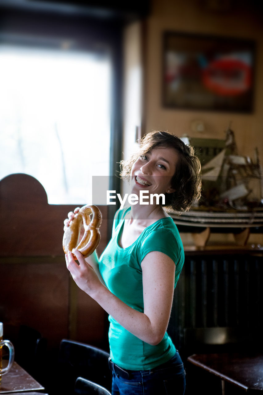 Portrait of smiling mid adult woman holding pretzel at home