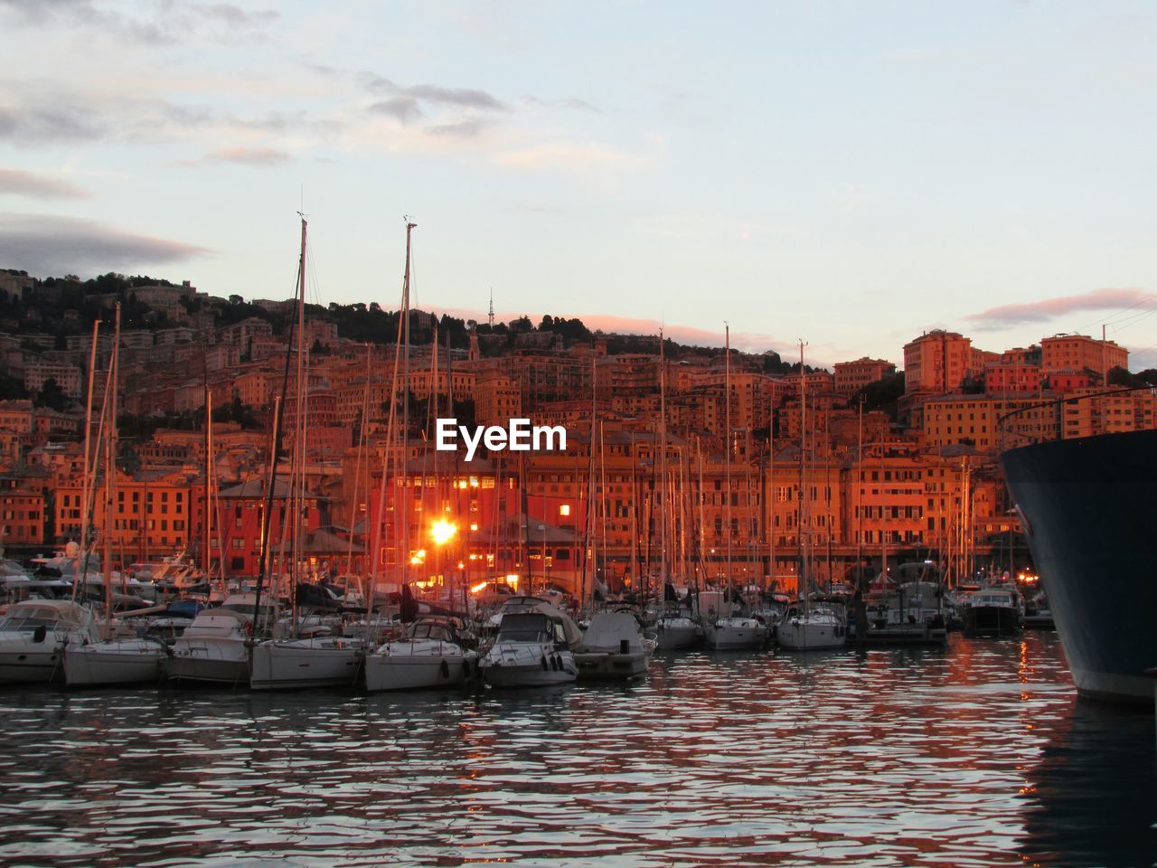 Sailboats moored at harbor against cityscape at dusk