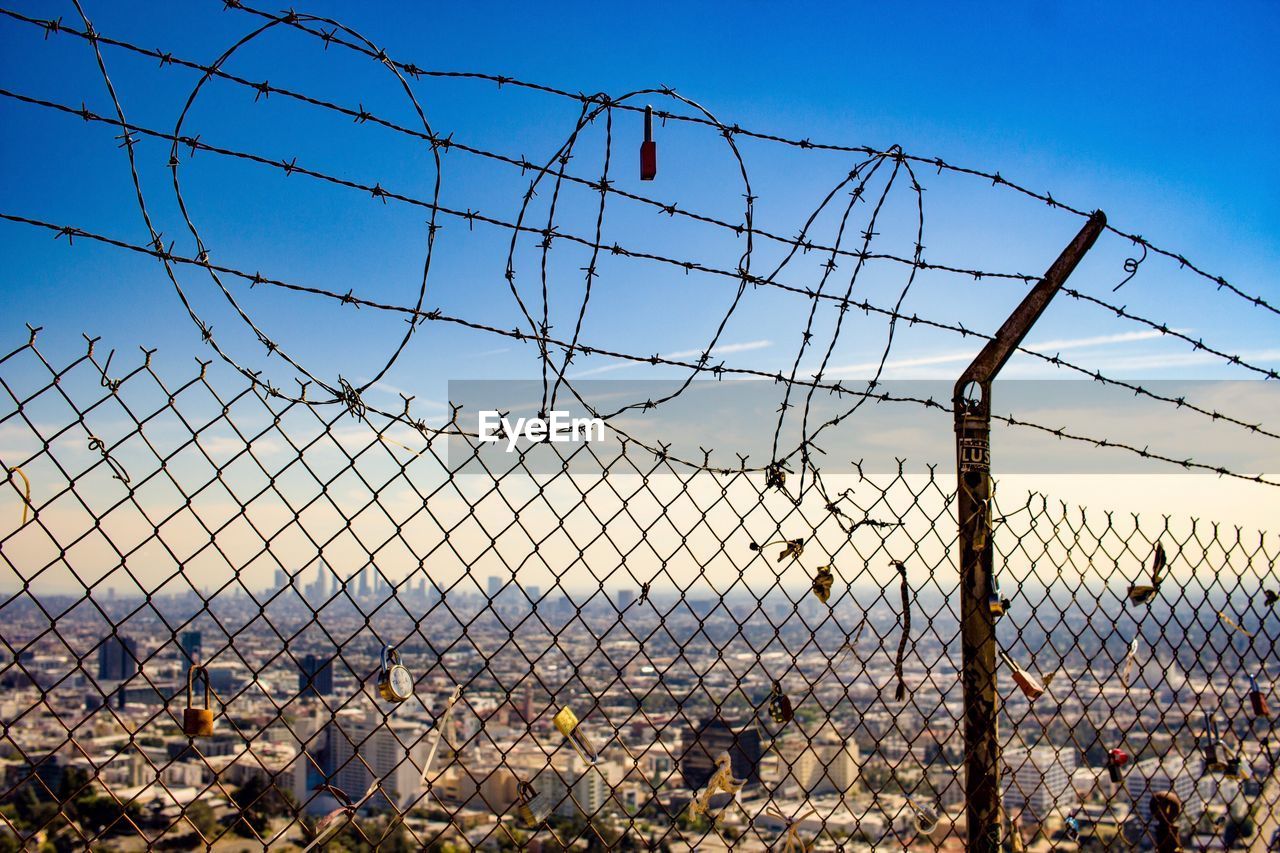 VIEW OF CHAINLINK FENCE AGAINST SKY SEEN THROUGH WINDSHIELD OF BUILDINGS