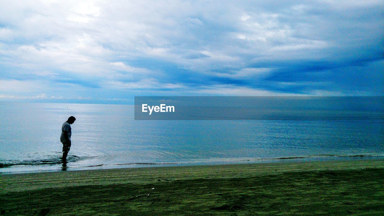 MAN SURFING ON BEACH AGAINST SKY