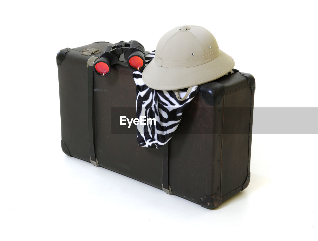 Close-up of luggage with hat and binoculars against white background