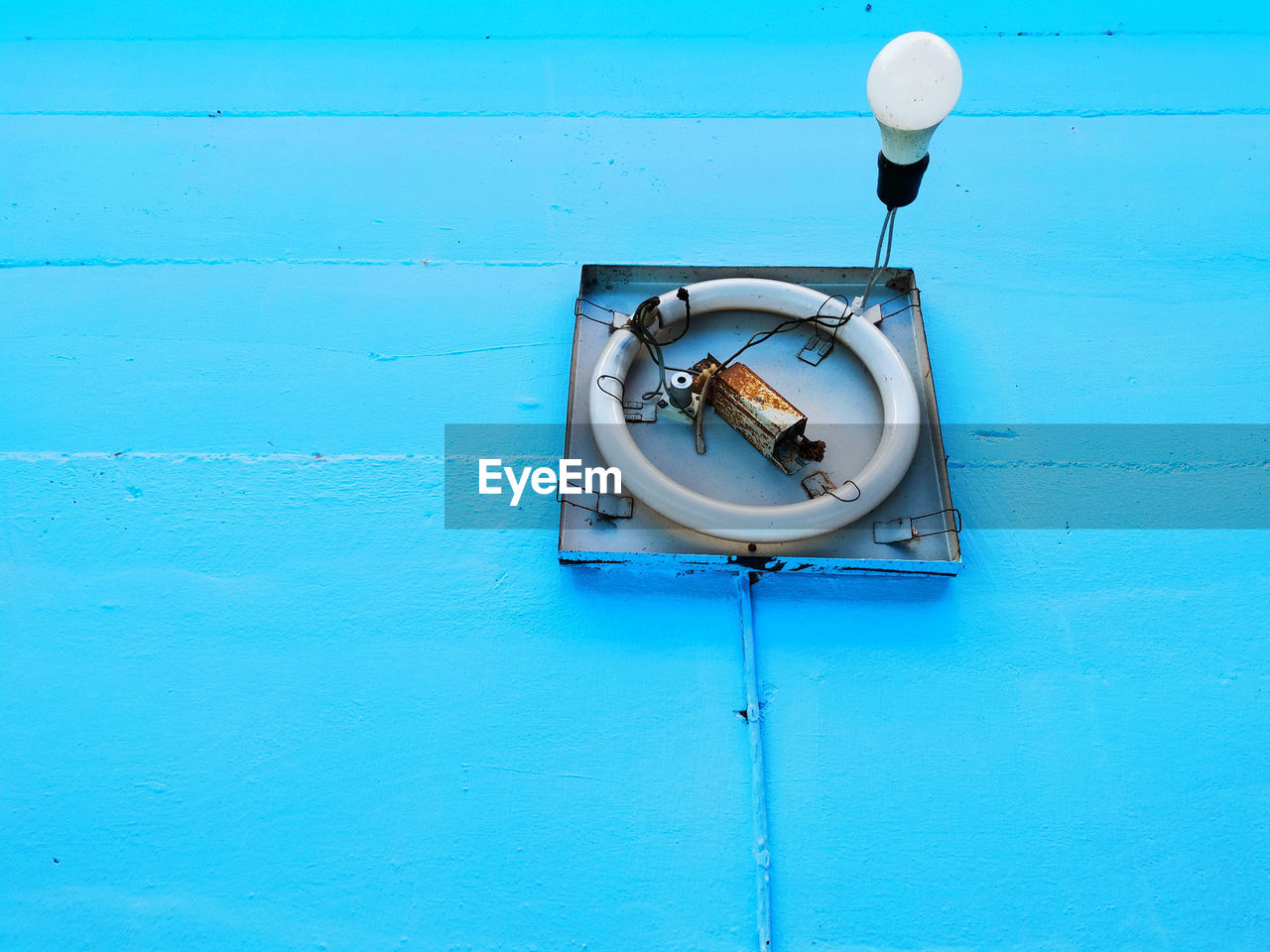 Close-up of electric lamp hanging against blue wall