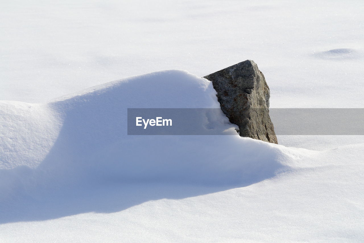 Scenic view of snow covered land with single rock
