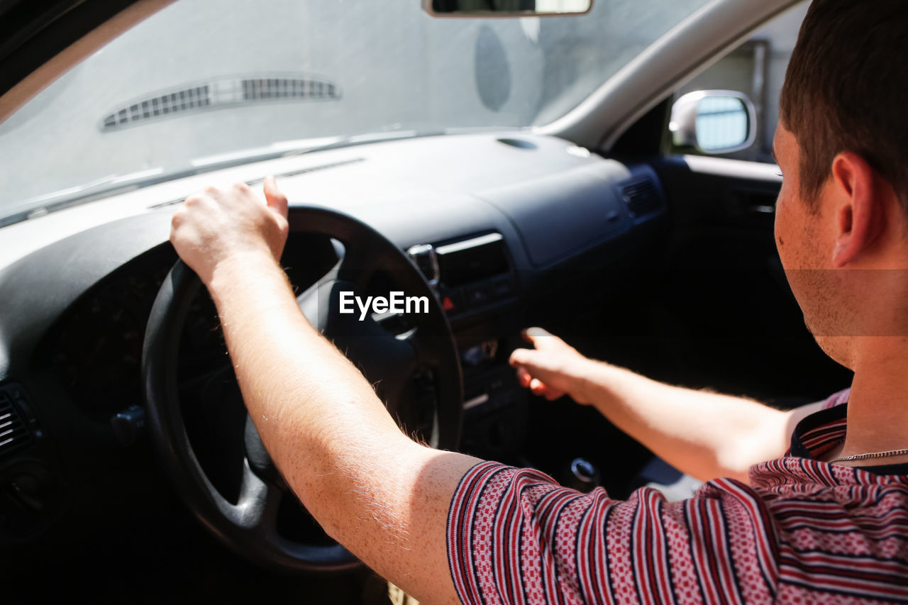 Caucasian young man sitting in car and driving. 20s guy looking from open window. silver grey 