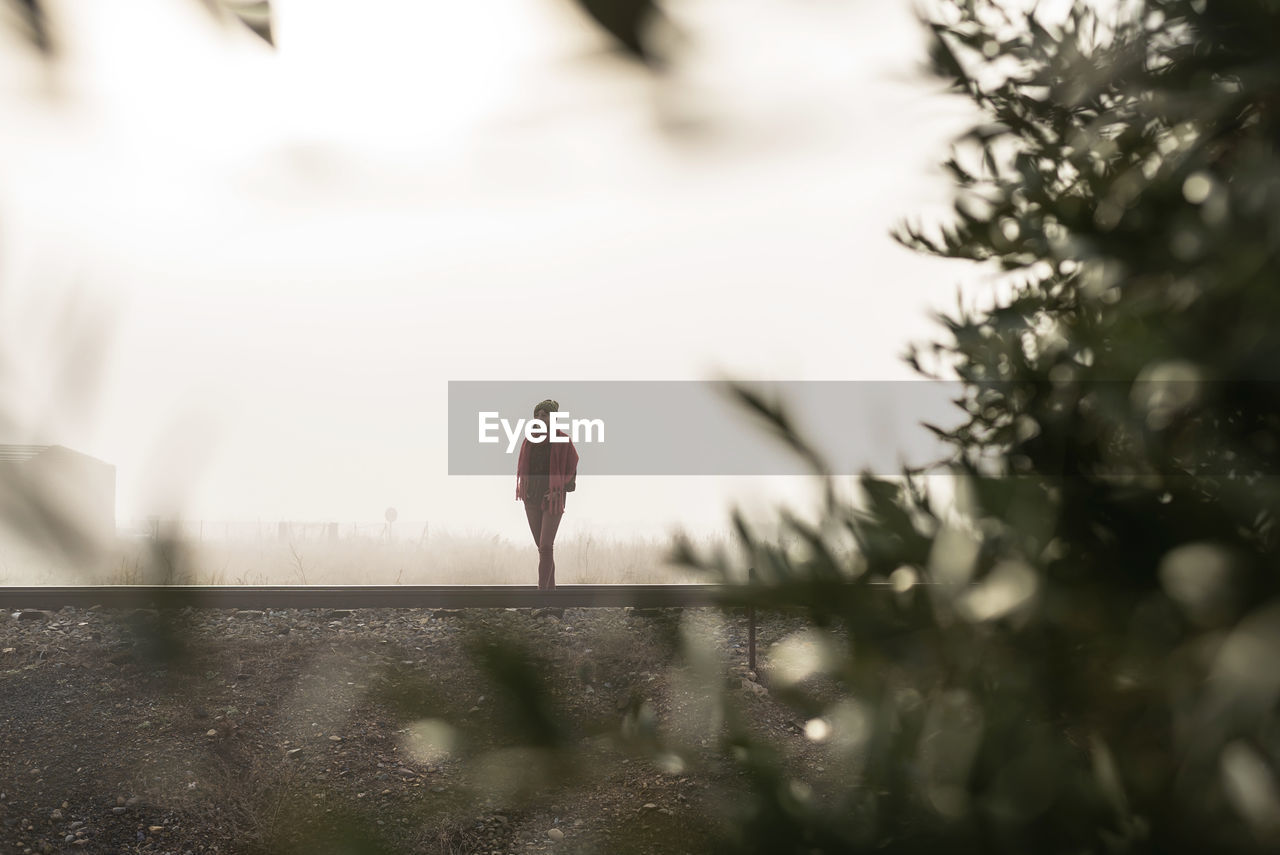 Thoughtful woman standing on a foggy railroad while looking away