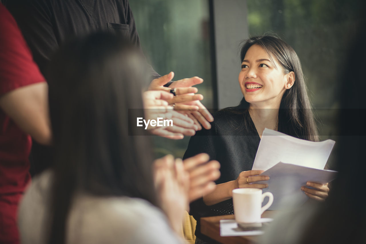 Woman holding papers by colleagues applauding