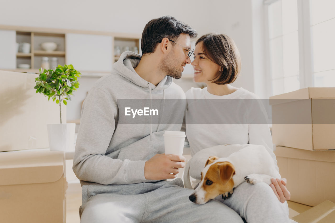 Romantic couple with dog sitting amidst boxes in new house