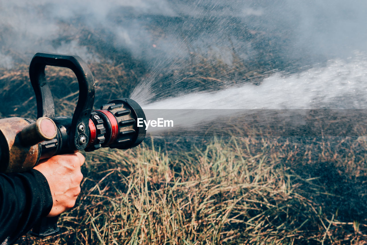Cropped hand spraying water in burning forest