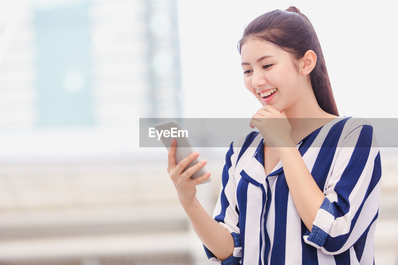 Smiling young woman using mobile phone while standing outdoors