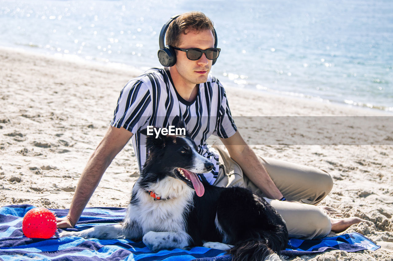 Relaxed man on the beach enjoying with his dog and listening to music with headphones