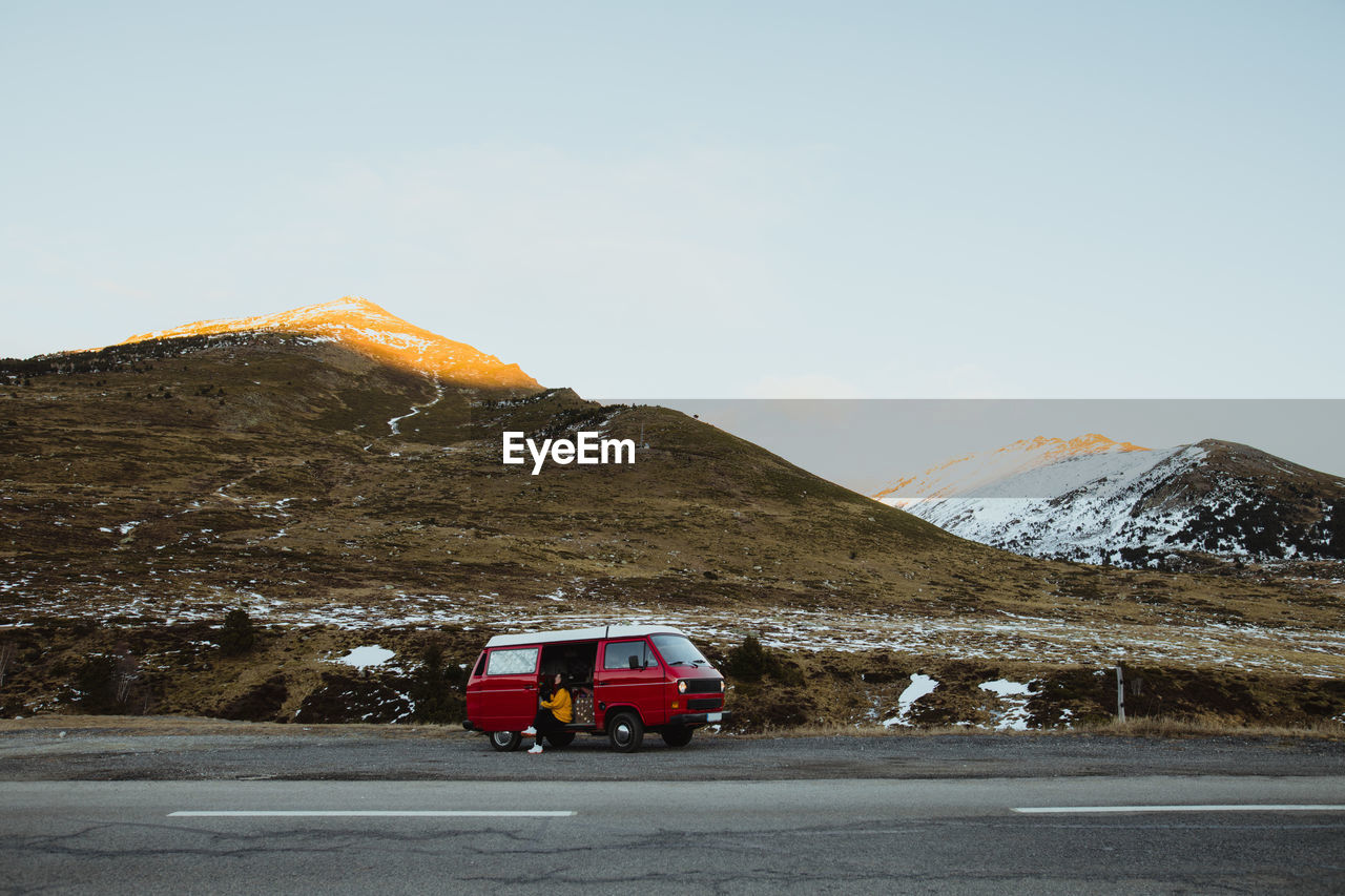 Young tourist in eyeglasses sitting in vintage automobile between deserted ground in snow near mountains