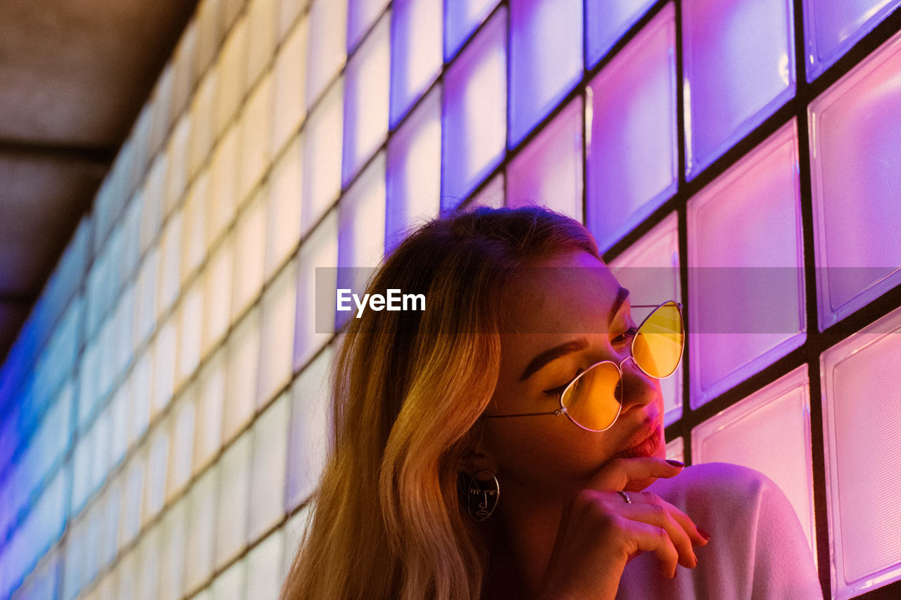 Young woman in sunglasses by illuminated wall